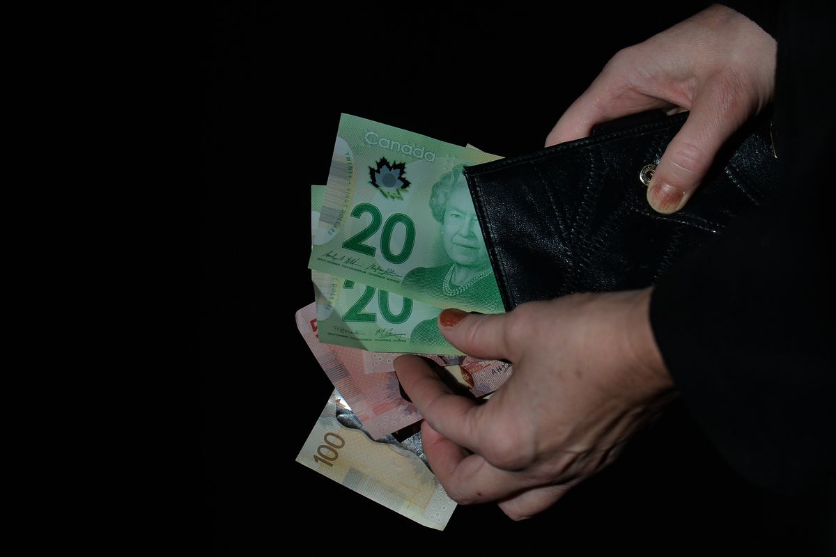 A close up of hands fanning out Canadian money from a wallet