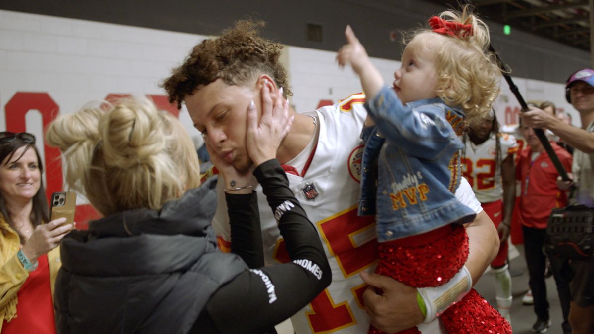 Patrick Mahomes holds his daughter and leans over to kiss his wife