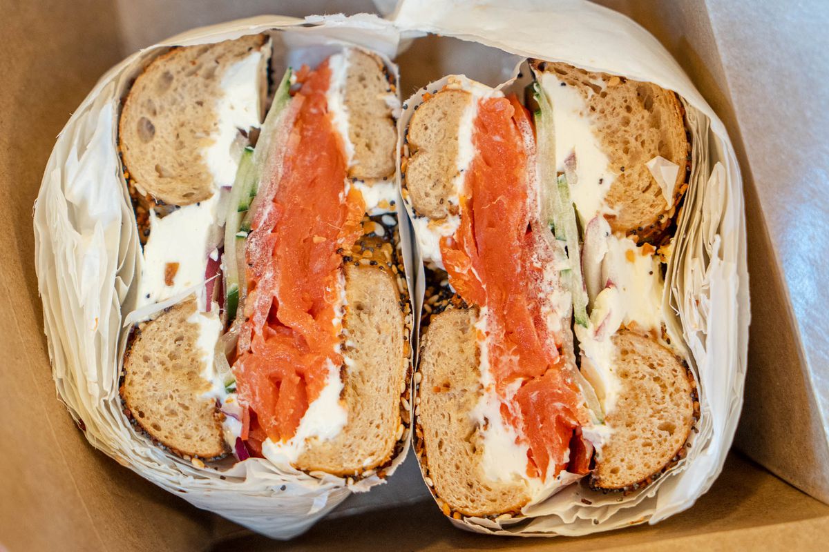 Two bagel halves filled with lox, cream cheese, cucumber, tomato, and onion.