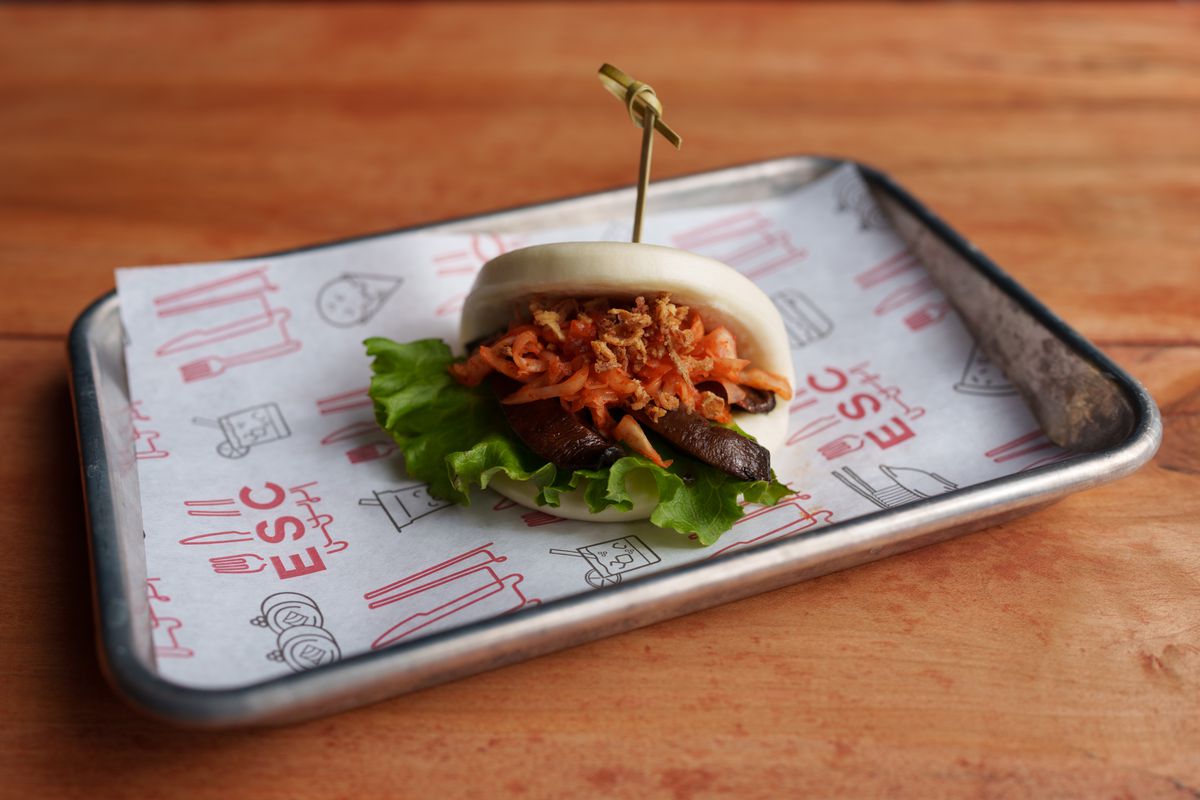 A bao stuffed with meat and veggies on a silver tray with paper on it. 