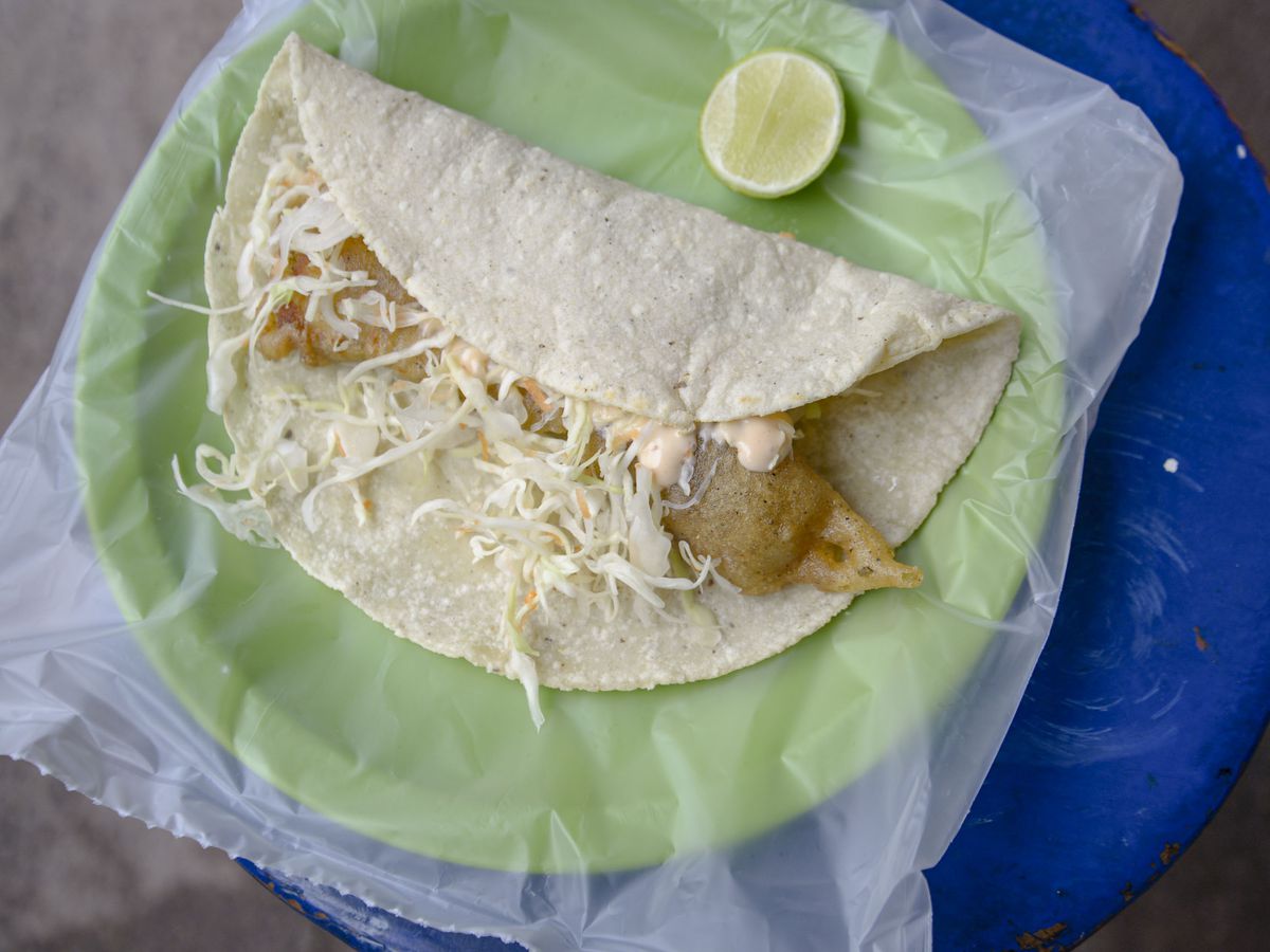 A fried fish taco on a plastic-lined plate with a wedge of lime.