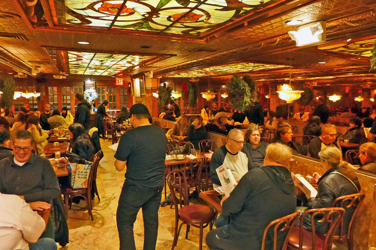 A room filled with patrons at small tables, with big mirrors on the walls.