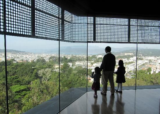 A person holds the hands of two children while staring out of floor to ceiling windows overlooking a view of San Francisco.