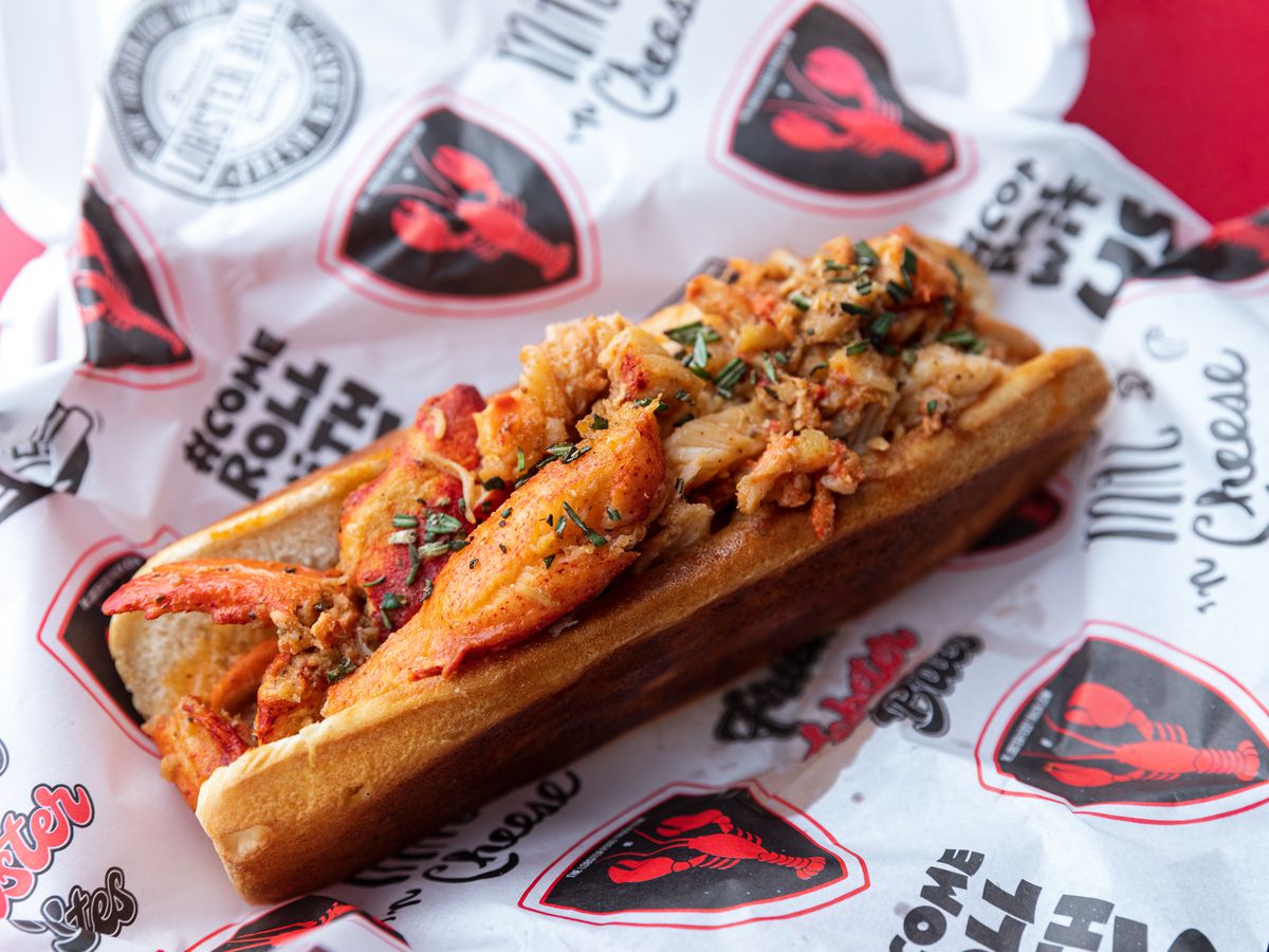 A bun with lobster stuffed inside sits on a piece of the Lobster Food truck branded paper.