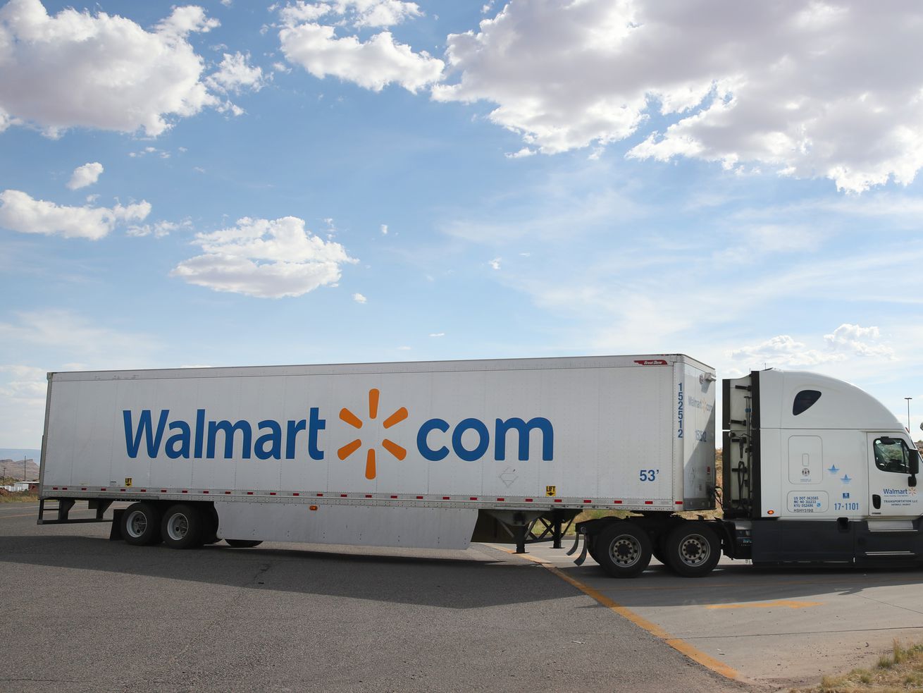 A Walmart tractor-trailer truck with walmart.com on its side leaves a parking lot.