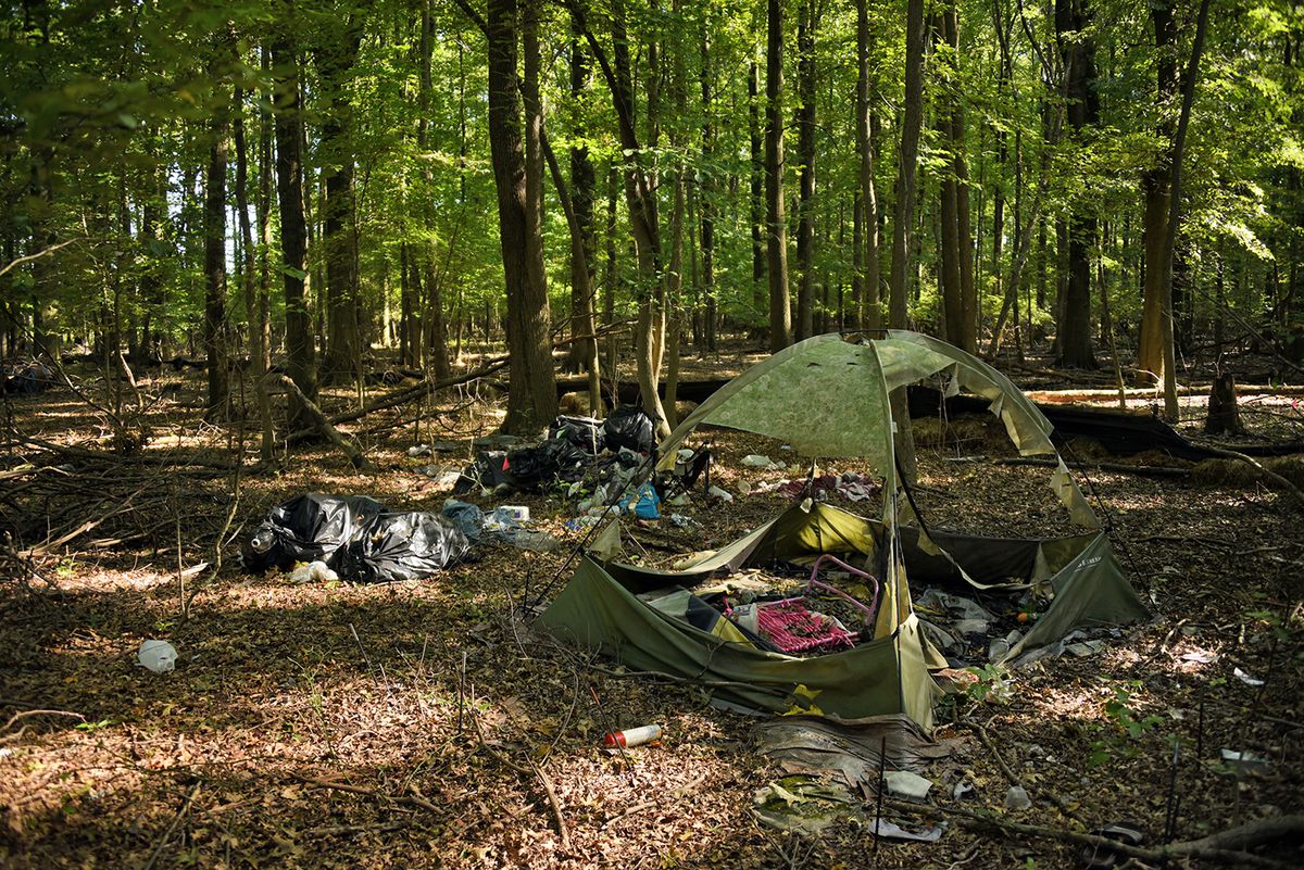 Trash in the middle of a clearing in a forest, including black garbage bags and a ripped tent. 