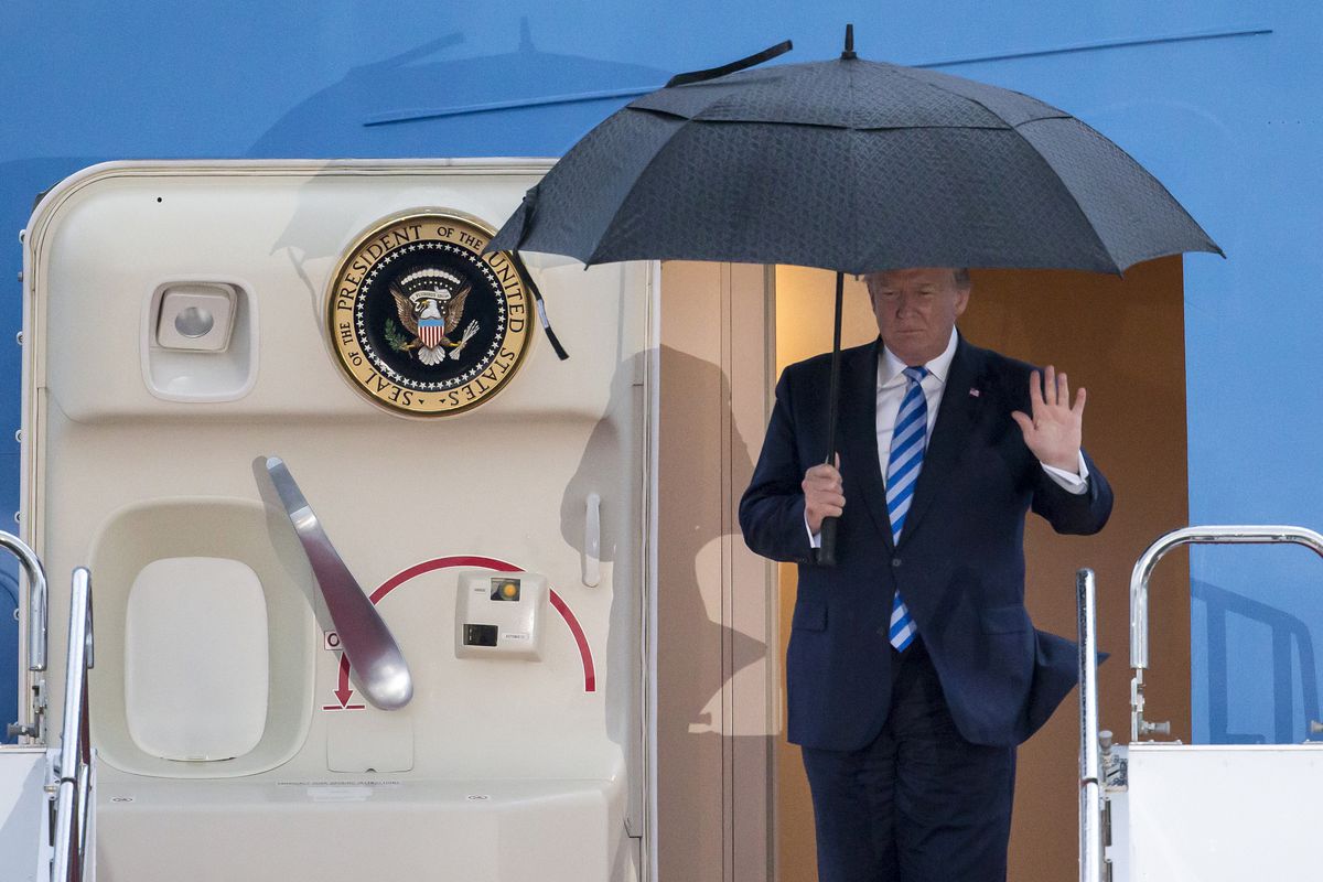 President Donald Trump steps off the Air Force One plane holding an umbrella over his head.