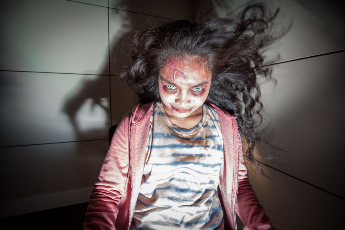 A demon girl (Erika Camacho) smiles menacingly at the camera as her hair blows back in Wellington Paranormal
