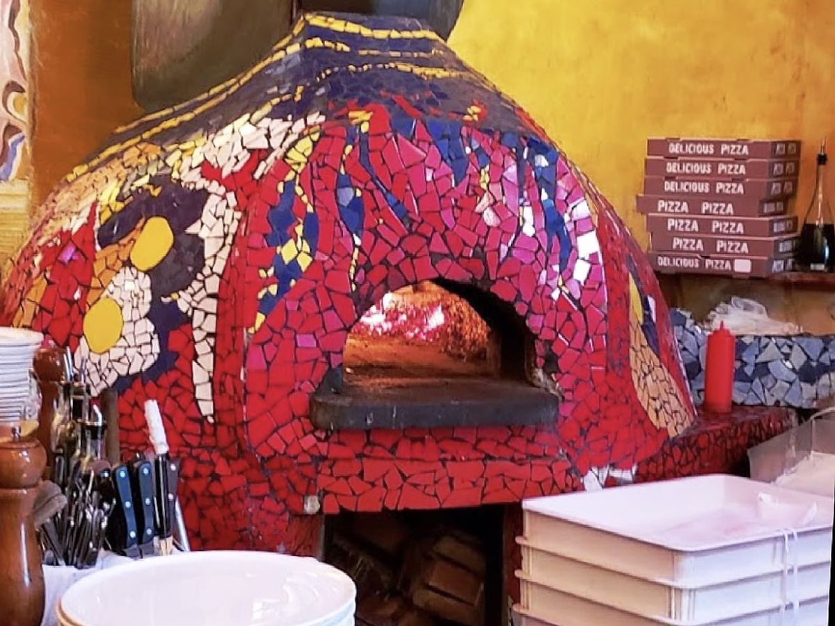A brick oven covered in pink, blue, and white designs, with pizza-making tools surrounding it.