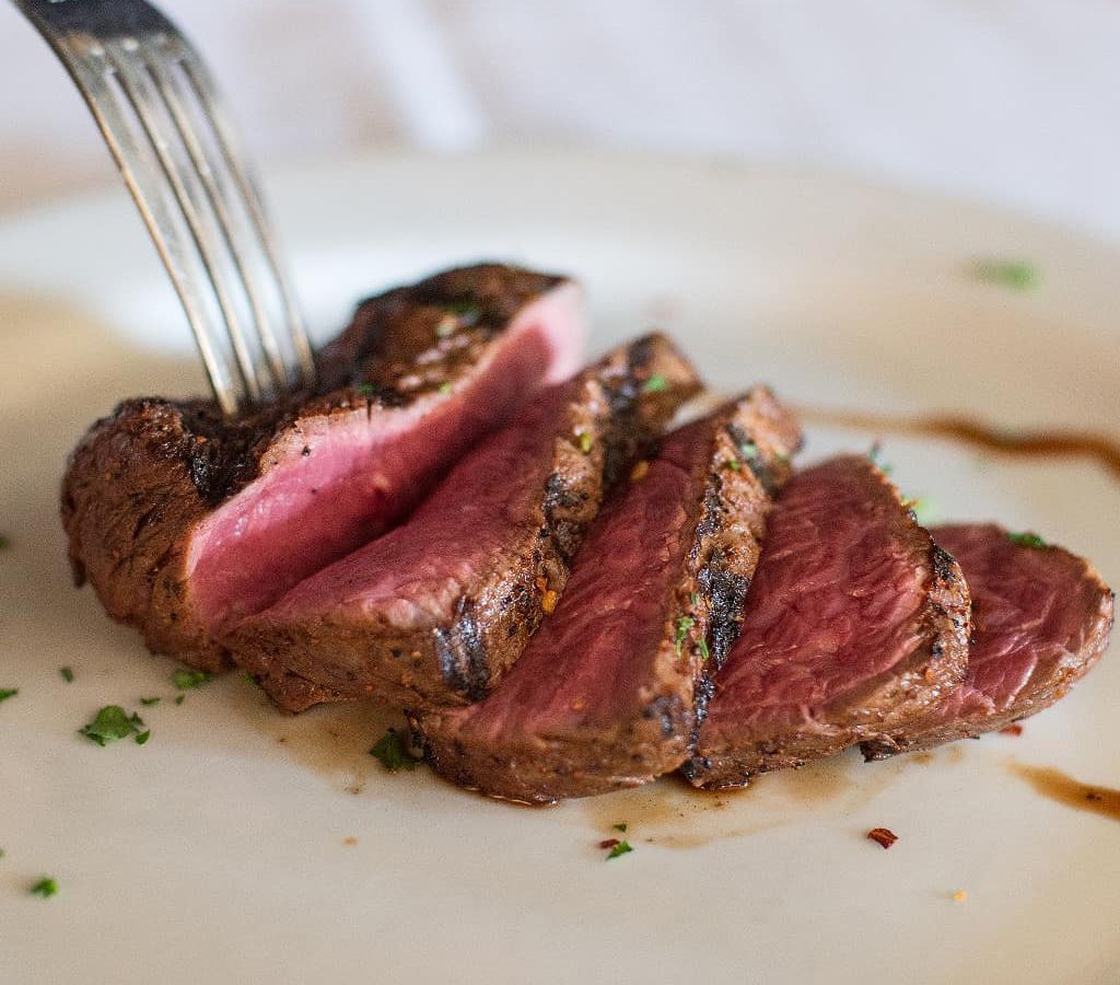 A fork piercing a piece of sliced steak on a plate.