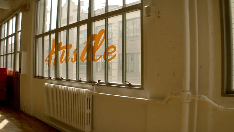 A window printed with cursive lettering reading “Hustle.”
