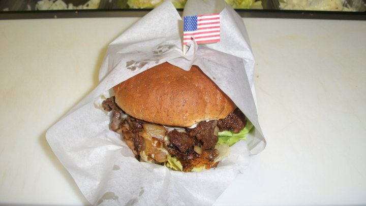 A bacon cheese burger with lettuce and tomato wrapped in paper and stuck with an American flag toothpick.