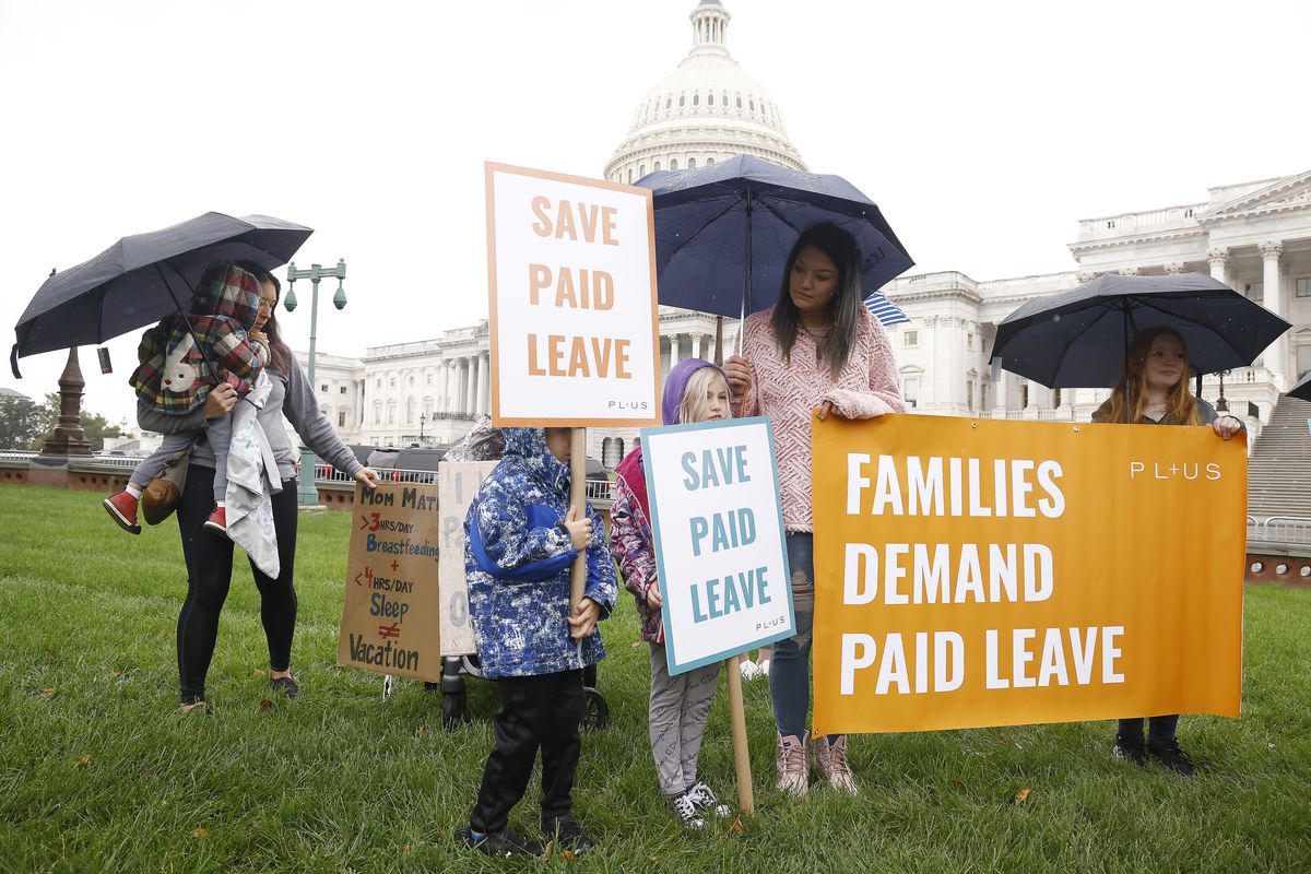 Adults and children carrying umbrellas over their heads gather on the US Capitol lawn carrying signs that read, “Families demand paid leave,” and, “Save paid leave!”