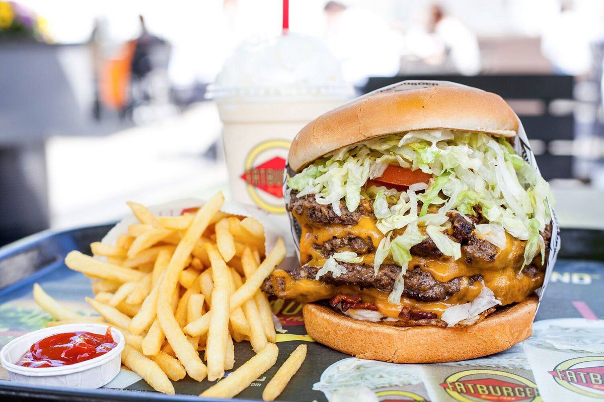 A very large burger next to fries and a milkshake.