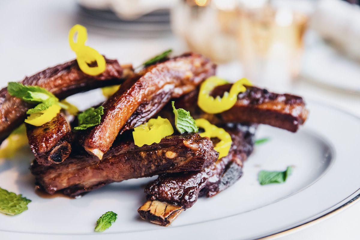 A plate of ribs stacked on top of one another and topped with slices of neon green pepper.