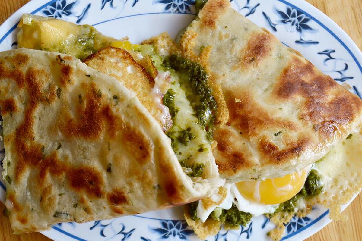 scallion pancake “sandwich” stuffed with greens and oozy eggs on a white plate with a blue floral border