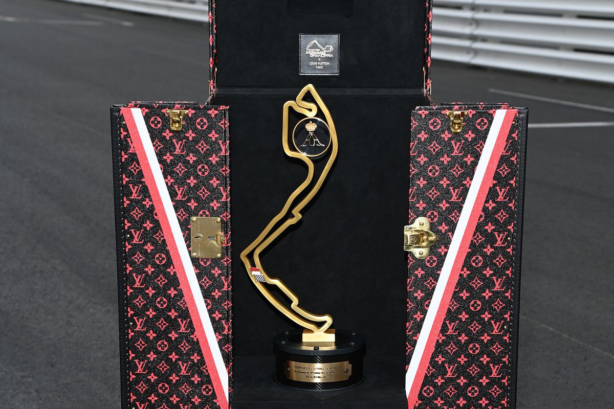 A picture of a trophy in the shape of the course of the Monaco Grand Prix in a fold out, Louis Vuitton case, printed with a pattern of a repeating Loui Vuitton logo