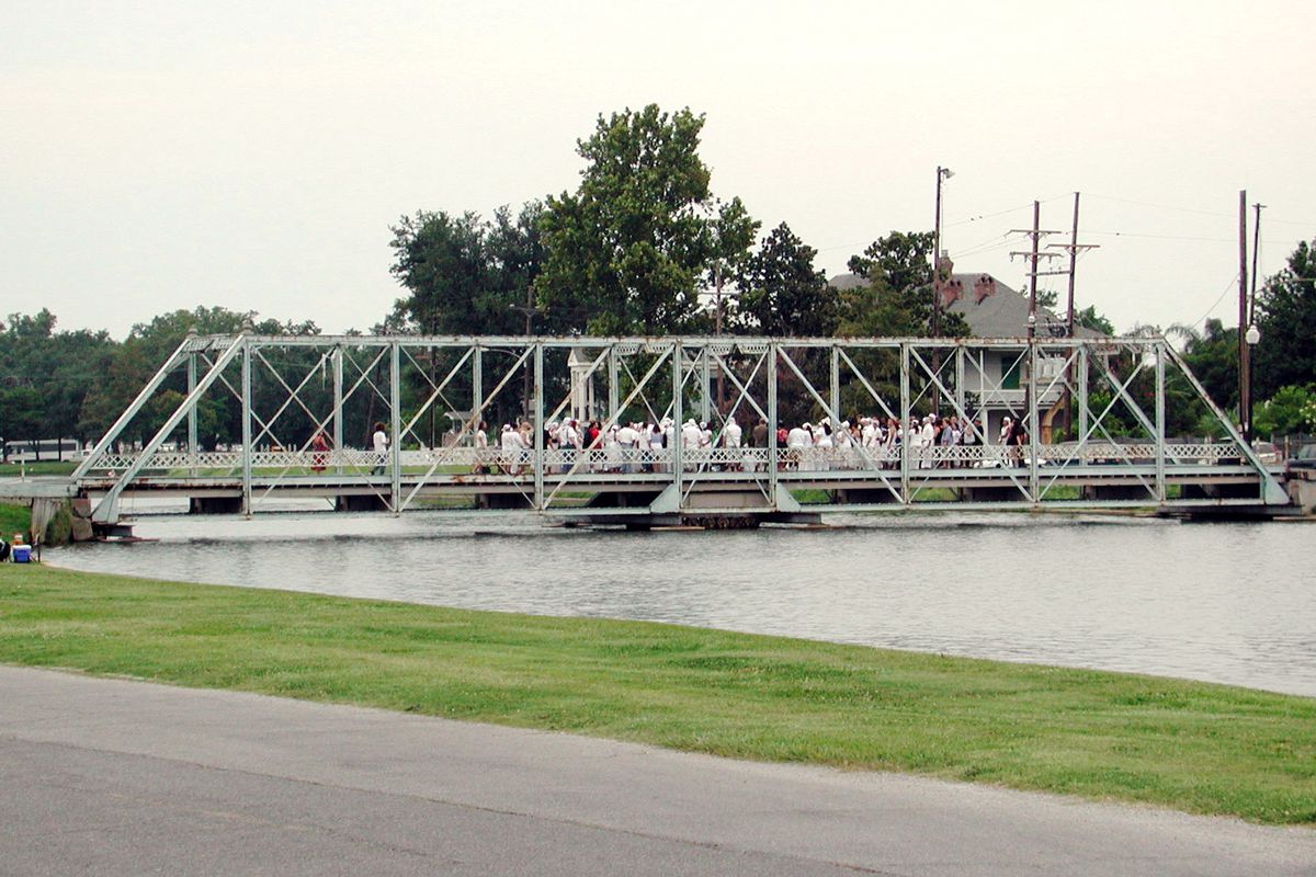 A pedestrian bridge spanning a small body of water. There are many people walking on the bridge.