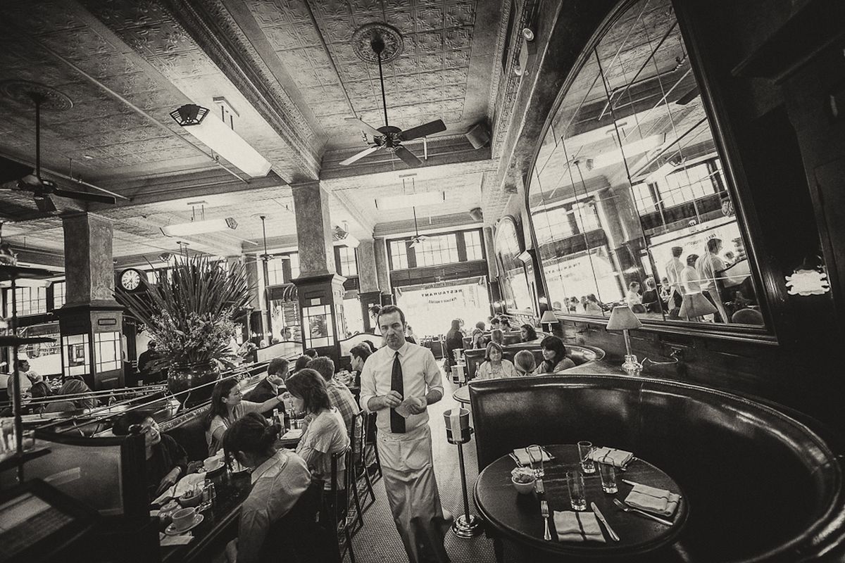 A black and white photo of a server moving through a crowded dining room.
