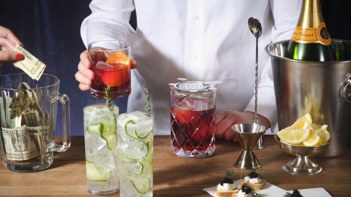 A bartender serves a negroni from behind a bar laden with cocktails and appetizers, while a hand drops a tip in a tip jar.