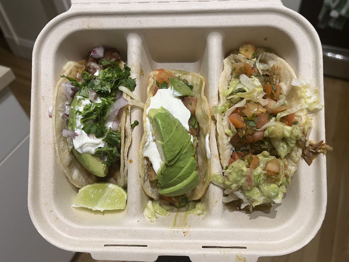 An opened box with three individual taco slots filled with tacos.