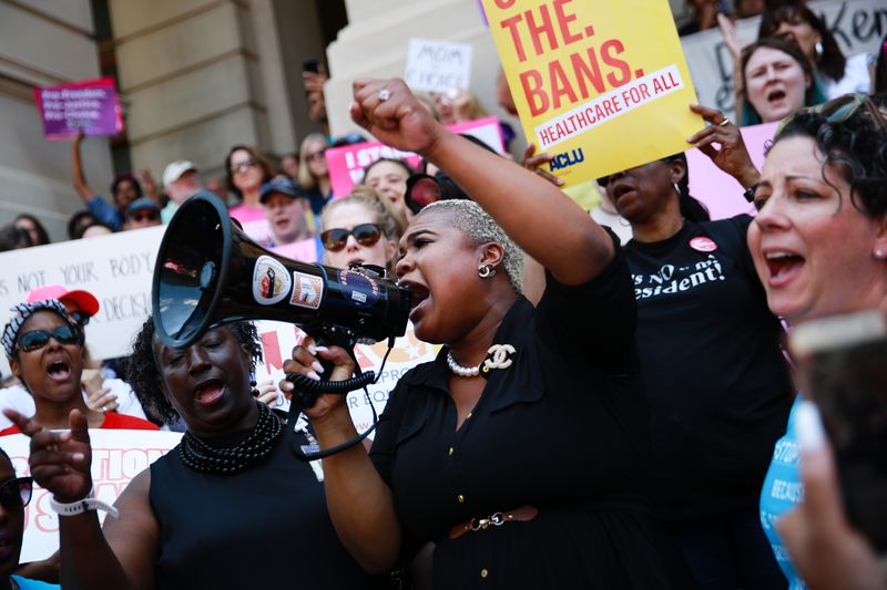 A Black woman with a megaphone speaks to a crowd of demonstrators on the steps of the Georgia State Capitol.