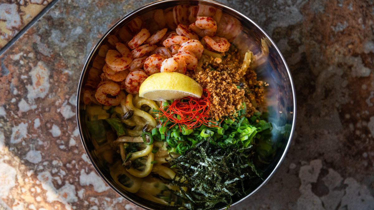 Butter udon noodles with poach shrimp, a lemon wedge, and herbs in a metal bowl. 