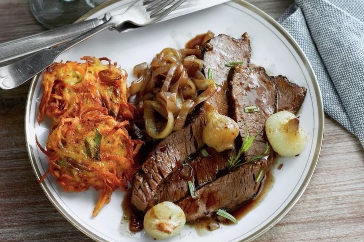 A plate of brisket with latkes, next to a glass of kosher wine.