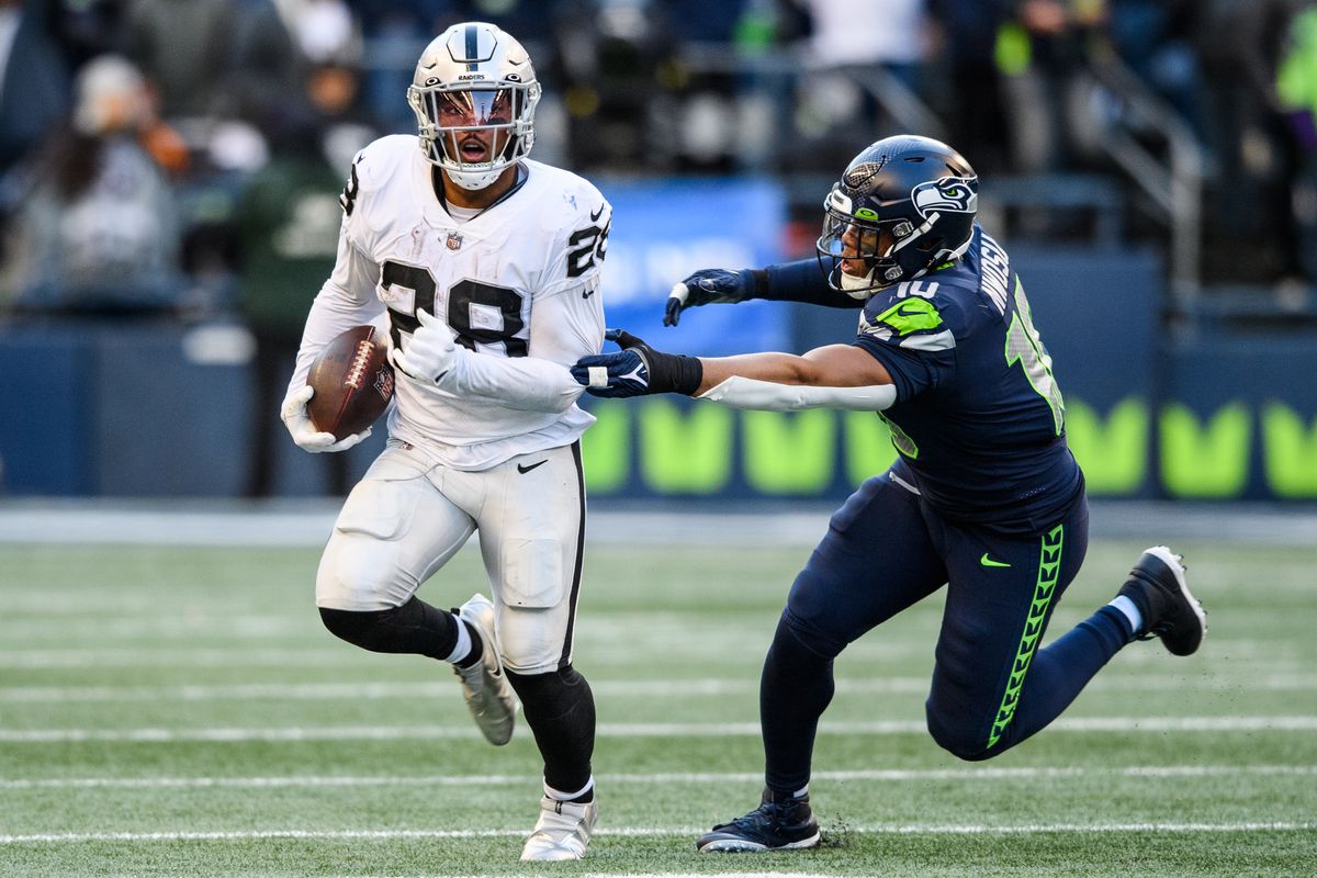 Josh Jacobs #28 of the Las Vegas Raiders runs with the ball while being chased by Uchenna Nwosu #10 of the Seattle Seahawks in the third quarter at Lumen Field on November 27, 2022 in Seattle, Washington.