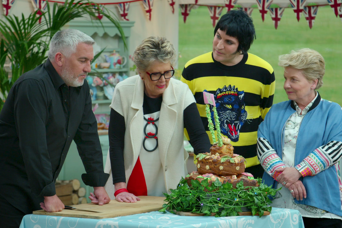 From left to right, Paul Hollywood, Prue Leith, Noel Fielding, and Sandi Toksvig stand at a table.