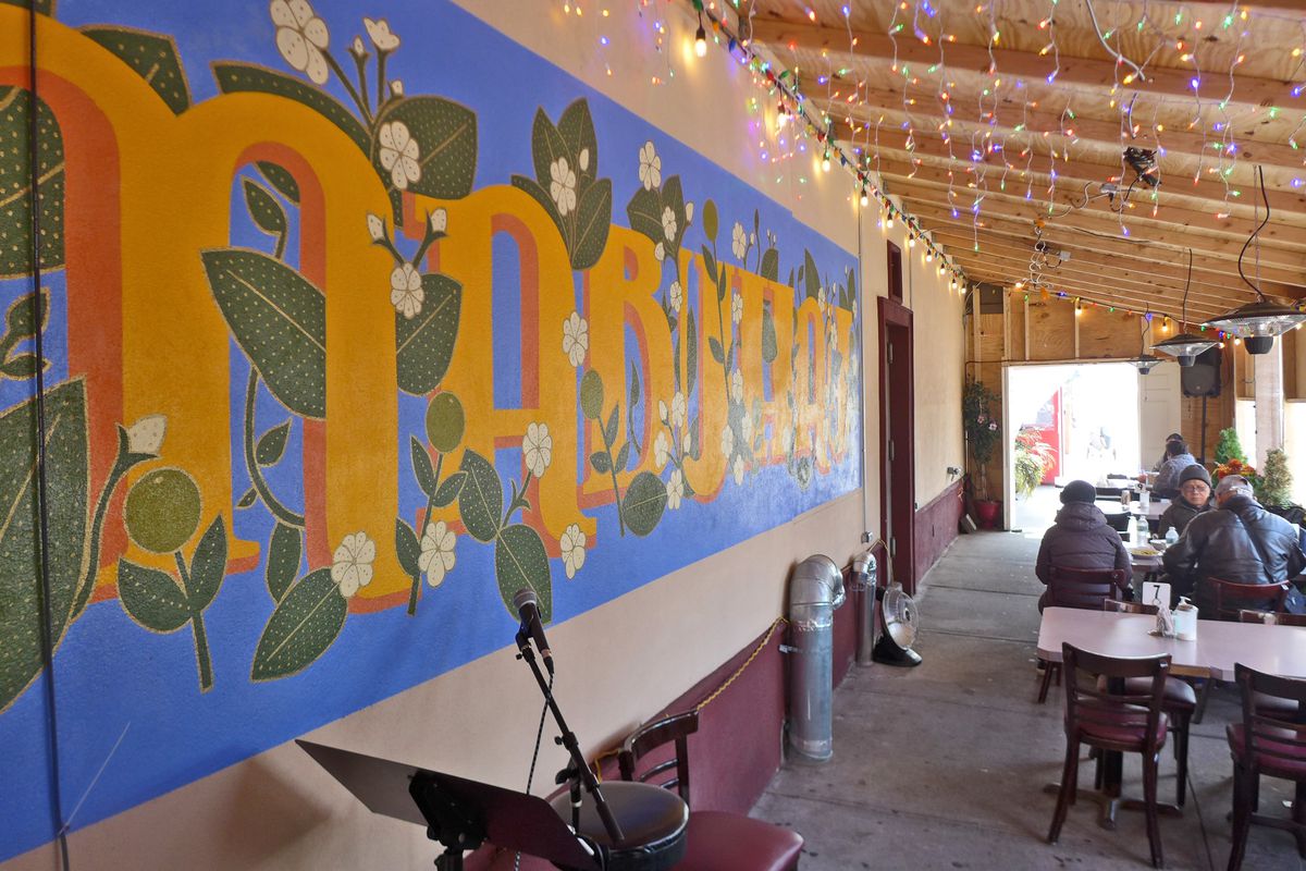 An outdoor seating area with mural on a wall to the left and customers seated at a table to the right.
