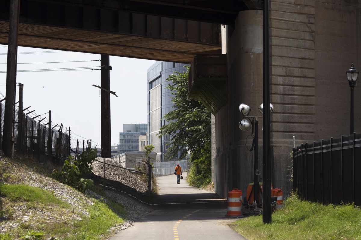 A two-way multiuse trail runs under an overpass. A man is seen walking on the trail in the distance.