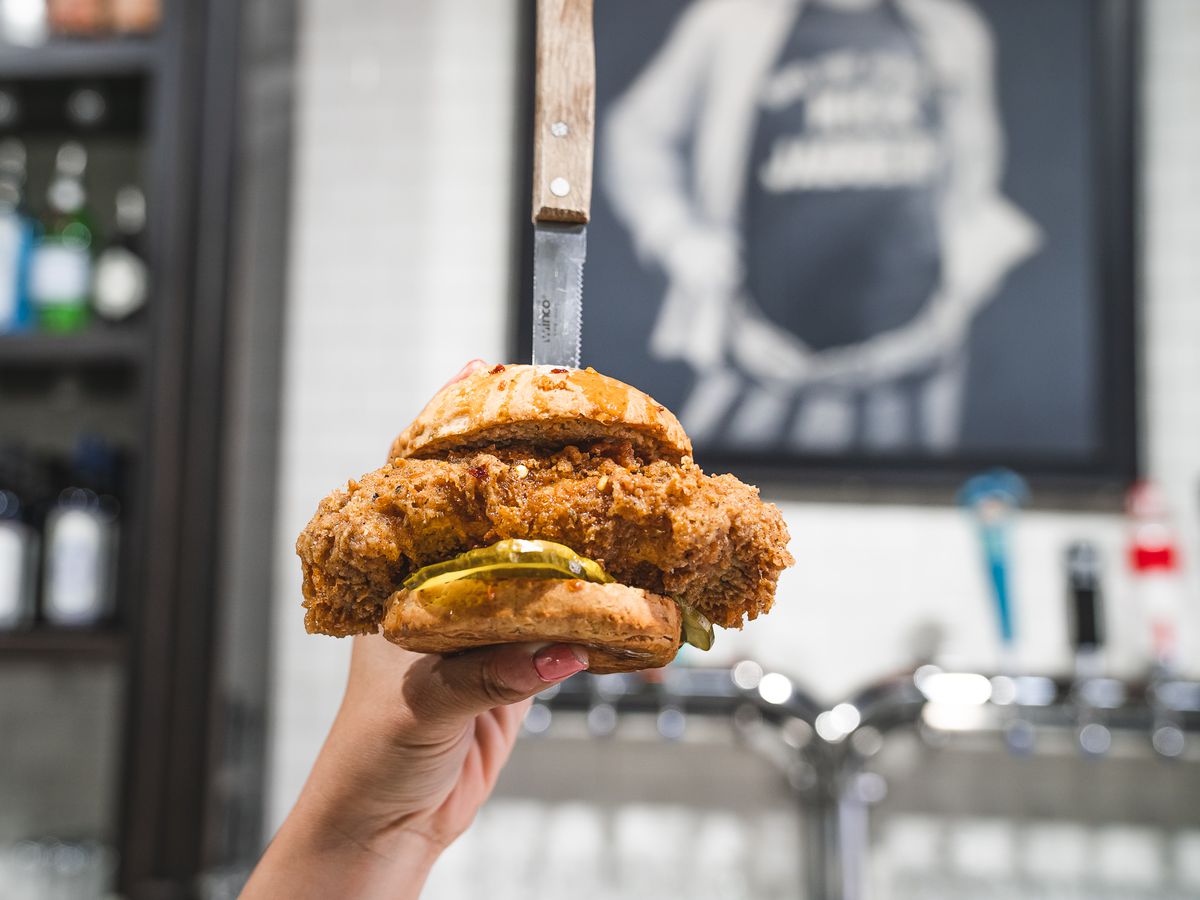 A hand holding a vegan chicken sandwich with a knife stabbed in the top of it