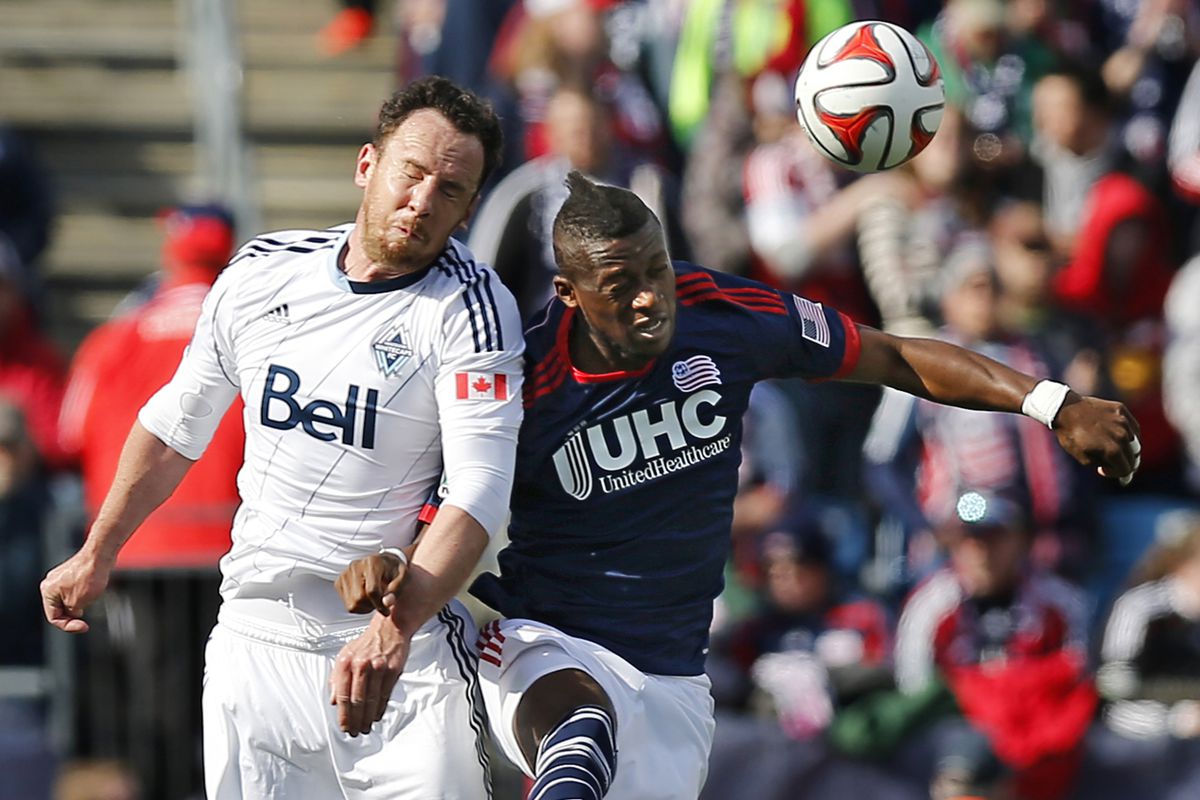 Vancouver centerback Andy O'Brien tangles with New England forward Dimitry Imbongo Boele.
