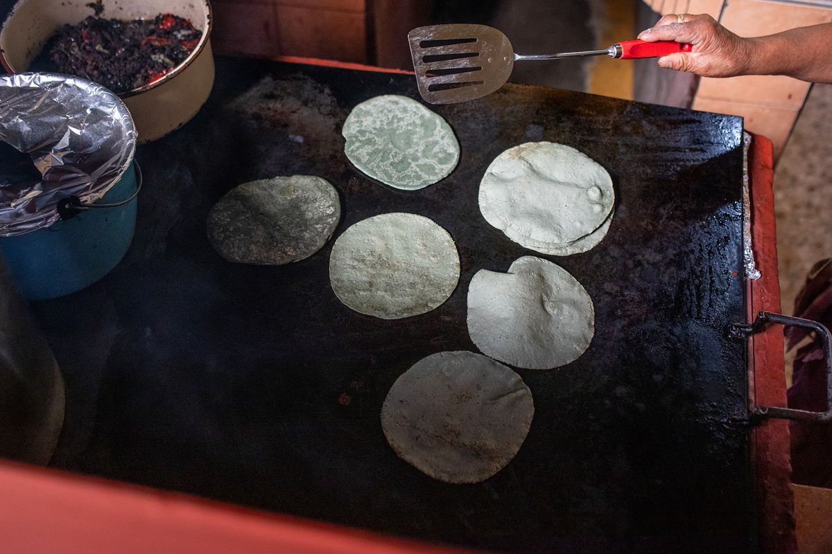 A hand uses a spatula to flip tortillas on a comal. 