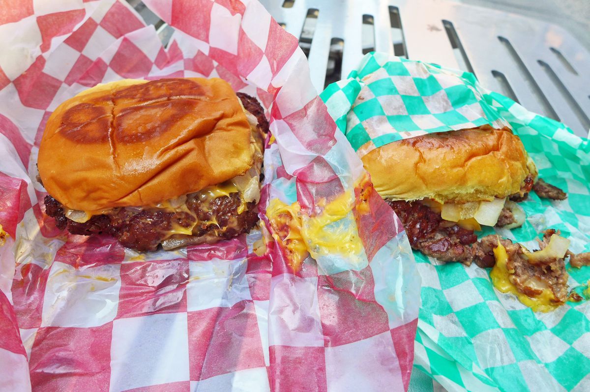 Two burgers on checked red paper and checked green paper.