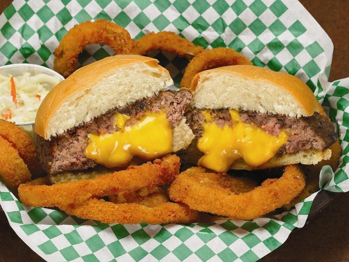 A cut in half burger stuffed with orange cheese in a basket with onion rings
