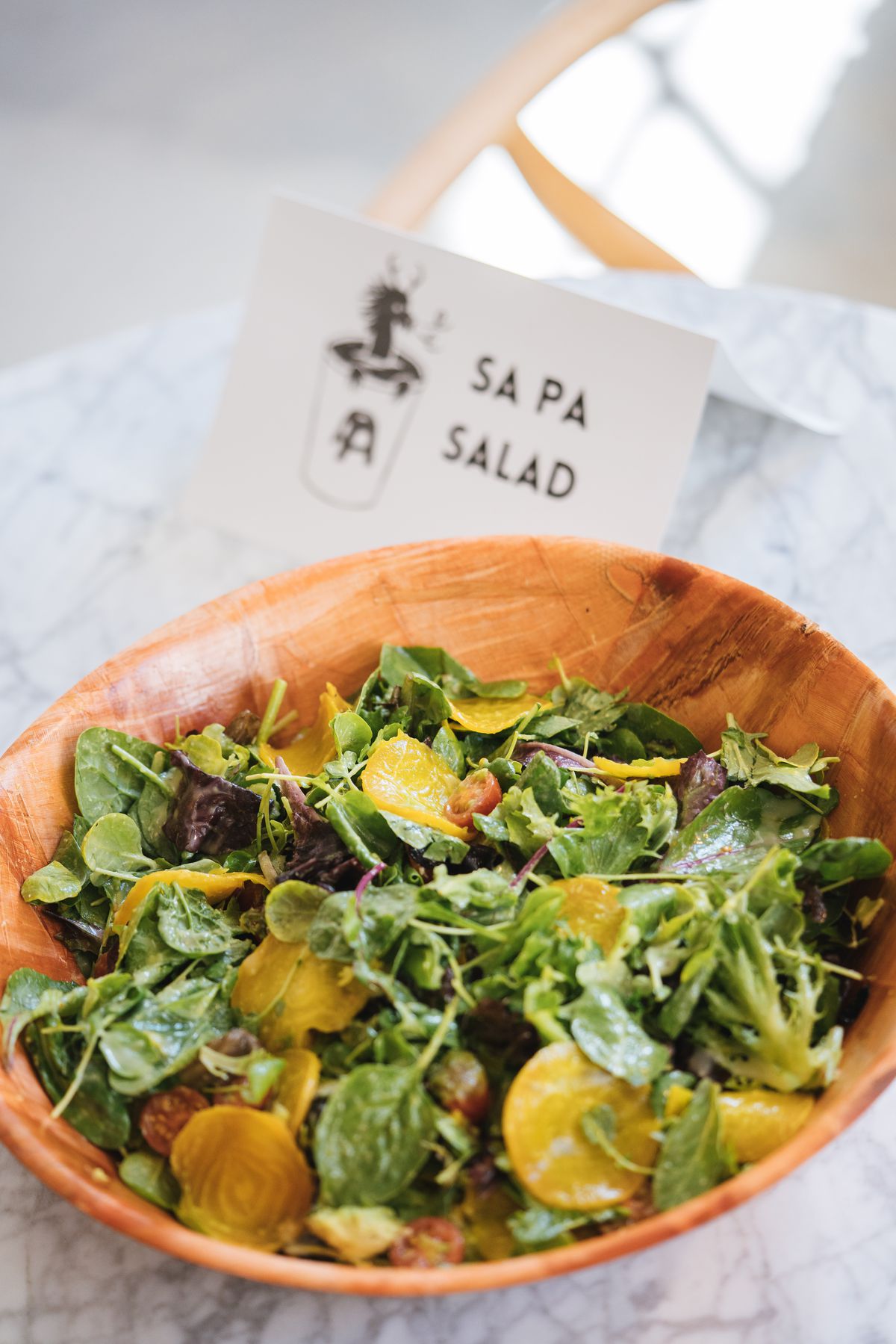 A salad with yellow beets in a brown bowl with a sign behind it that says Sa Pa Salad.