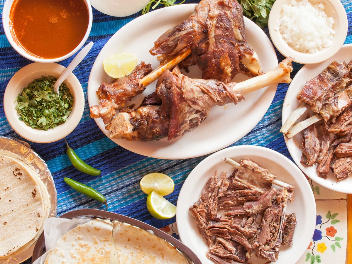 An overhead shot of roasted meat on bone with broth and tortillas.