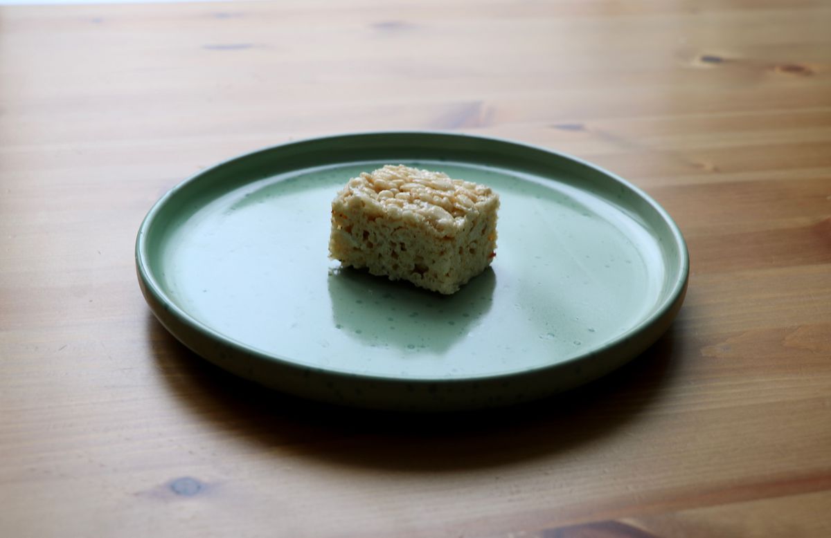 A Rice Krispies Treat sits on a teal plate against a light wooden background