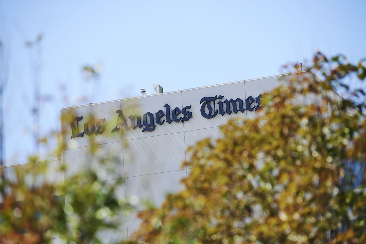 Signage of the Los Angeles Times on the side of building shrouded by trees.