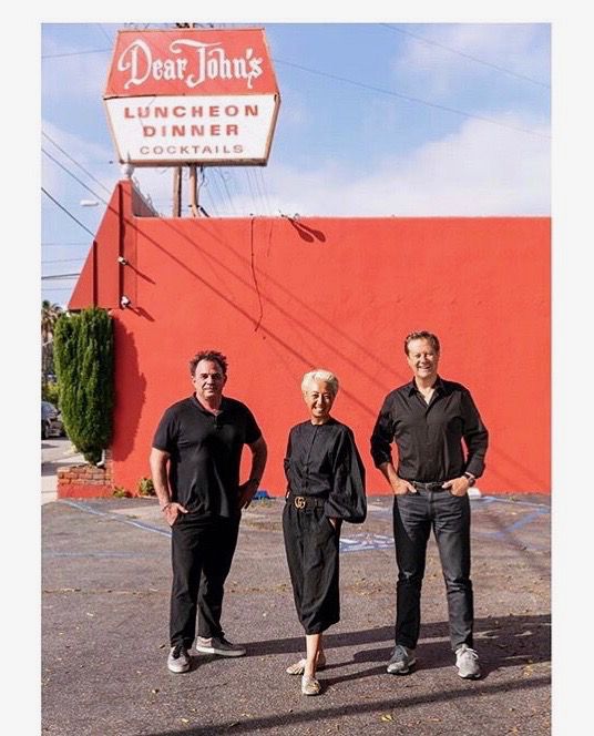 A trio of owners in black outfits stand in front of their red restaurant.