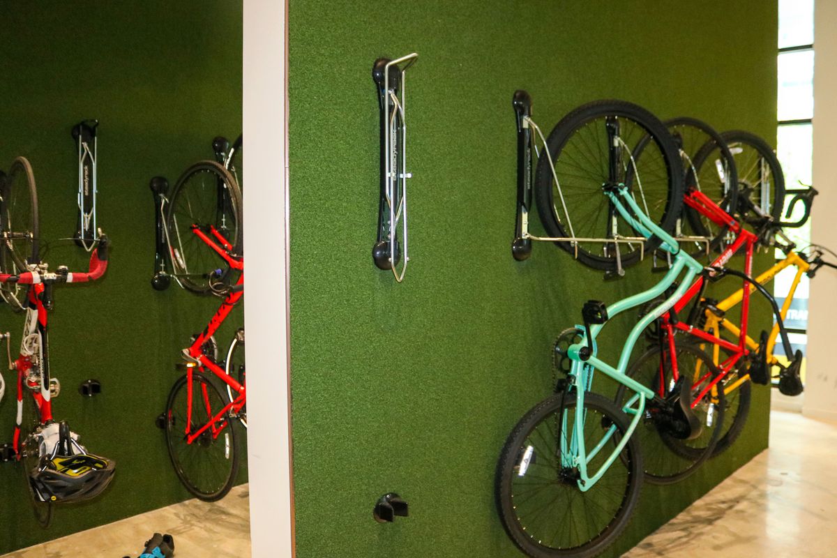 A room with many bikes hanging from a green wall. 