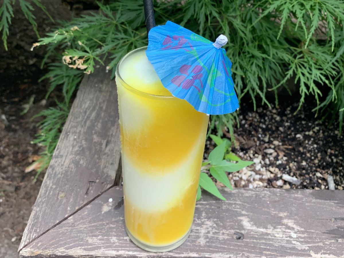 An orange-and-white blend of two slushies, adorned with a blue umbrella, sits on a planter outside Gold Dust Meridian in Portland.
