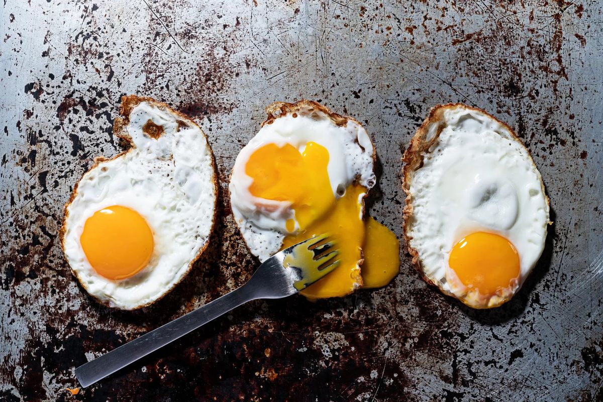 Three fried eggs on a griddle, one with its yolk broken by a fork.