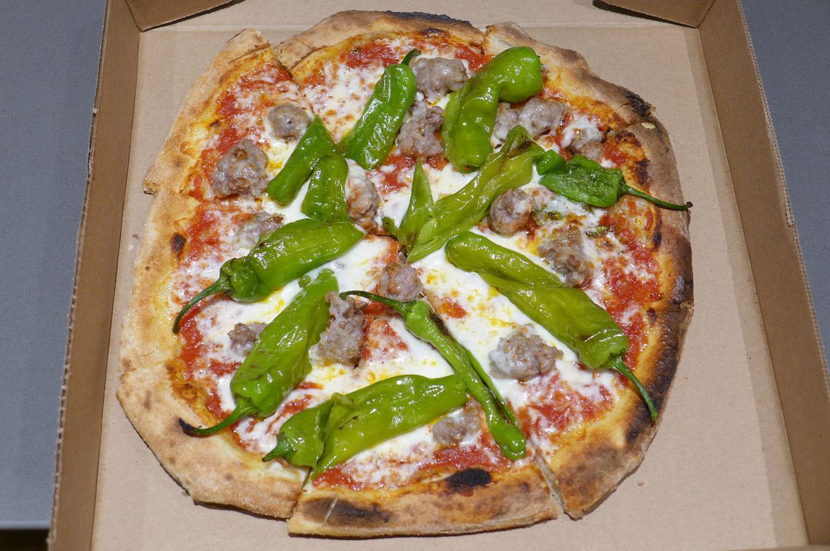 Green peppers, sausage chunks, and cheese on an irregular round pizza.