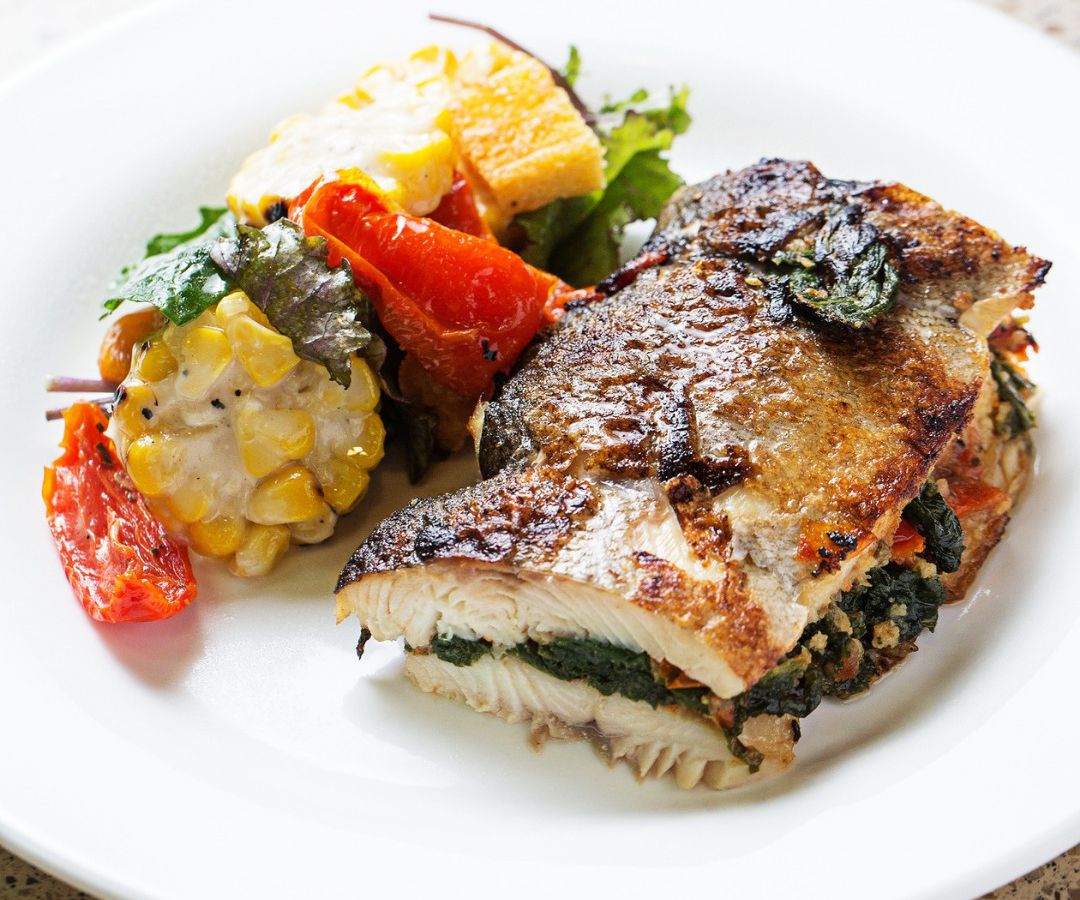 A colorful medely of vegetables next to a seared and stuffed fish dish.