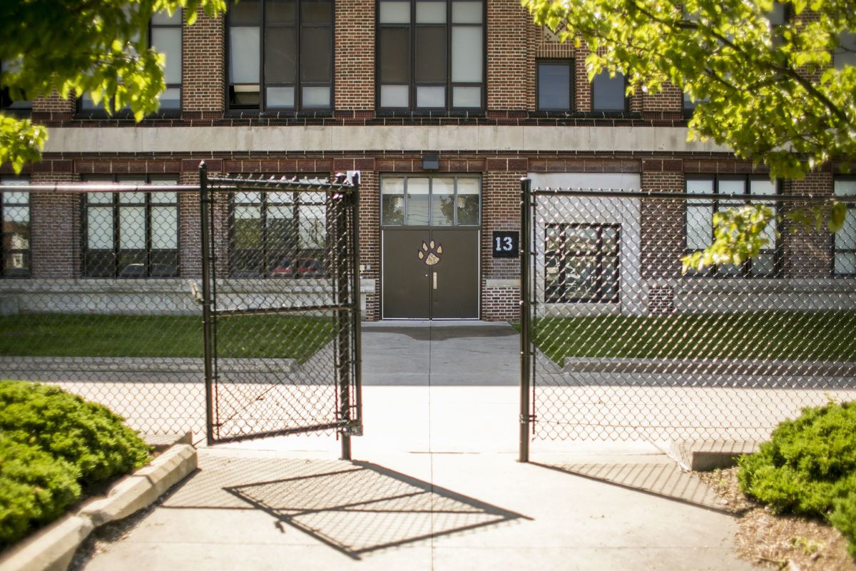 Detroit’s Southeastern High School, a large brick building surrounded by a chainlink fence. There is a logo of a yellow paw print on the door.