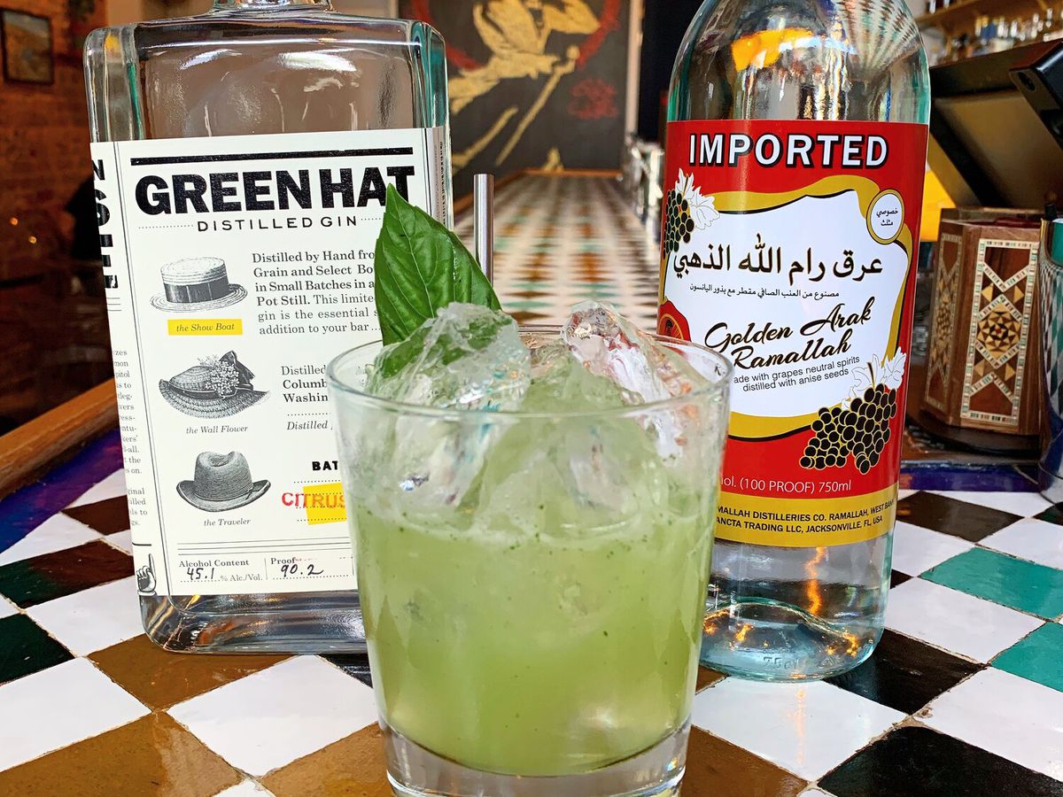 An almost neon green cocktail with Green Hat gin in the background.