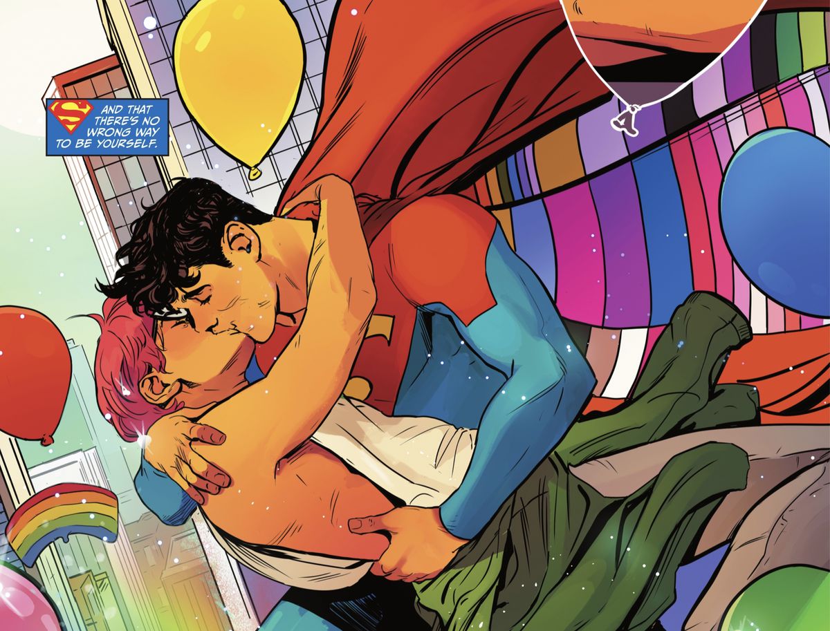 Jay Nakamura and Jon Kent/Superman kiss in DC Pride 2022. Jon is wearing his Superman costume with a cape lined with the colors of many LGBTQ Pride flags. From DC Pride 2022.